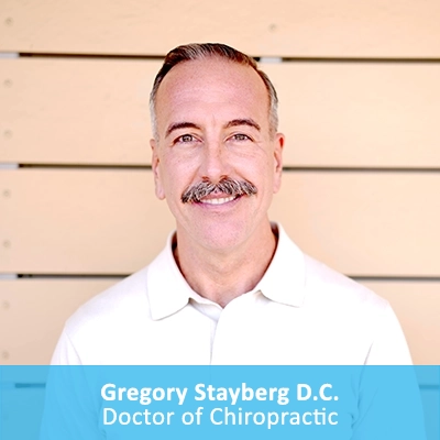 Chiropractor Gregory Stayberg Smiling In Front Of Wooden Wall With Caption